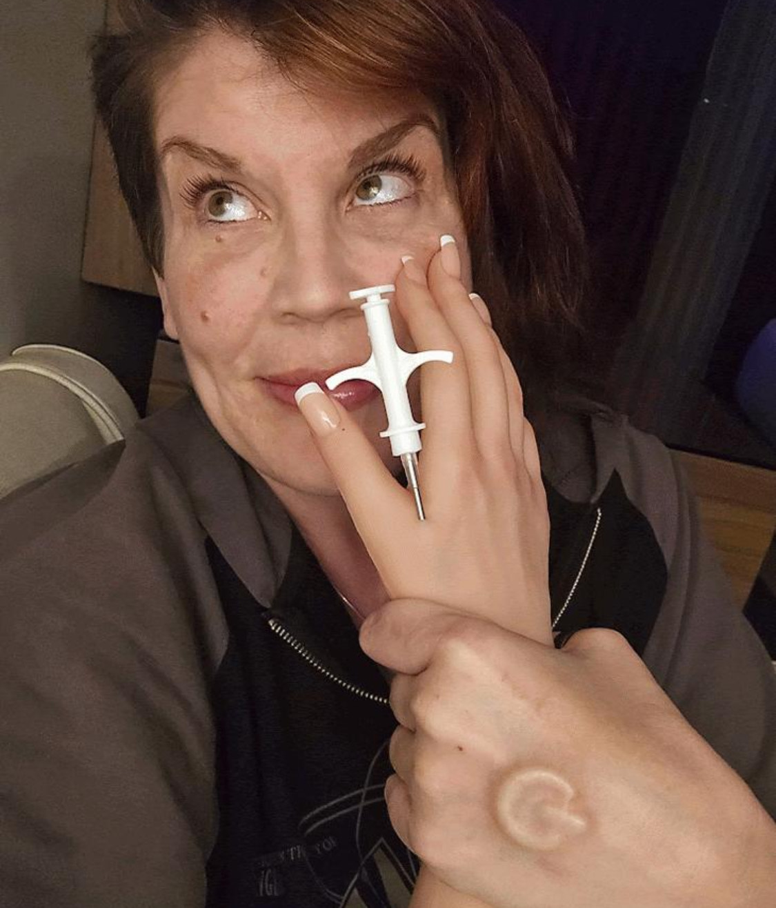 Anastasia Synn holds up her left hand, which has a syringe with a large needle inserted between her thumb and pointer finger.